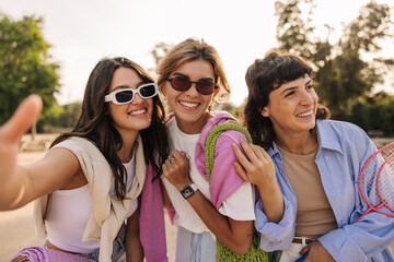 Happy young caucasian ladies smile with teeth relaxing outdoors on warm day. Girlfriends wear casual clothes, sunglasses in summer. Weekend concept.