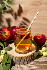 Glass of apple juice and apples in the garden under sunlight. The concept of harvesting the autumn harvest of apples vertical photo