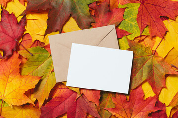 Naklejka na ściany i meble Festive card with envelope template with fallen autumn dried leaves background. Autumn mood design mockup. Colorful, variegated foliage. Flat lay, top view, copy space.
