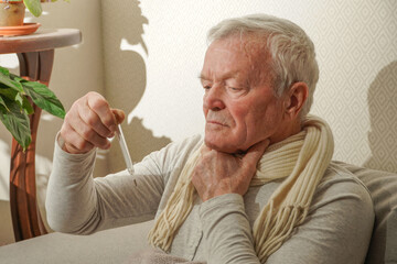  Sick senior man using thermometer checking his temperature suffering from seasonal flu or cold.