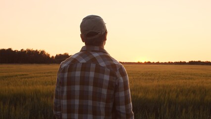 Farmer in front of a sunset agricultural landscape. Man in a countryside field. Country life, food production, farming and country lifestyle concept. - obrazy, fototapety, plakaty