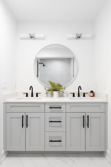 A renovated bathroom with a grey vanity cabinet, circular mirror with a view to a shower, and back...