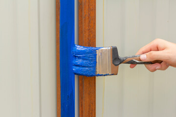 Painting rust with blue paint for metal.The hand paints the crossbars of the fence.