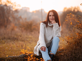 Smiling young brunette woman in a white warm sweater. Autumn time , a sunny portrait at sunset