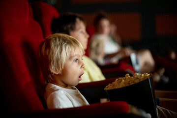Cute child, boy, watching movie in a cinema, eating popcorn and enjoying