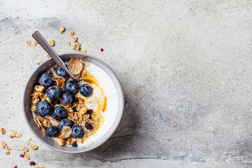 Breakfast yogurt bowl with granola, blueberries and maple syrup, gray background.