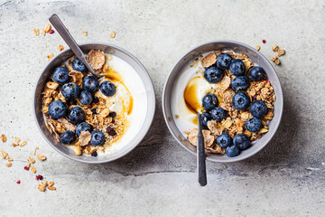 Breakfast yogurt bowl with granola, blueberries and maple syrup, gray background.