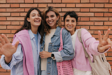 Happy young caucasian ladies in good mood posing against backdrop of brick wall. Girlfriends blonde, brunettes wear light casual clothes. Spring season concept