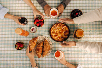 Top view of covered table tablecloth with cake, croissants, berries and picnic drinks. Female young...