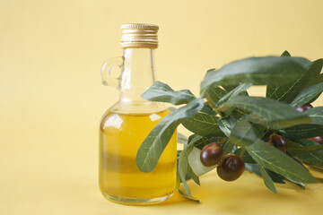 bottle of olive oil and fresh olive leaf on yellow background 