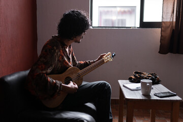 A young Mexican musician is tuning his jarana guitar before composing a song at home