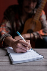 An young Mexican musician is writing a song in his notebook while holding his jarana guitar