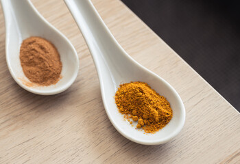 Two spoons with spices on a table. Cinnamon and Indian curry
