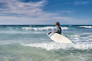 Curly man wearing wetsuit preparing enjoying of the wavy sea with his surfboard