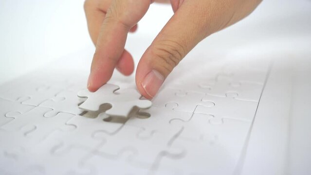 hand is picking up a white jigsaw puzzle and attaching it to the board