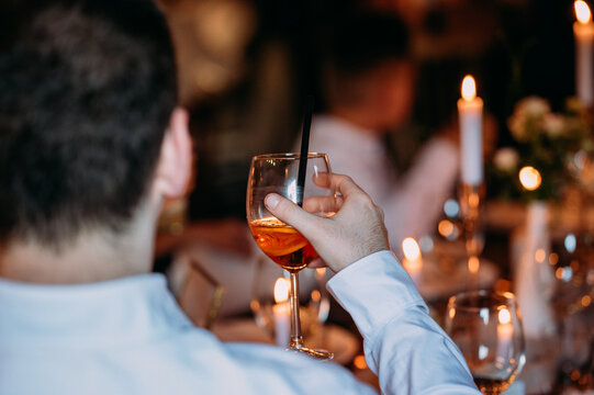 Abendliches Ambiente auf einer Hochzeit - Ein Mann hält ein Glas Wein hoch zum anstoßen bei Kerzenschein