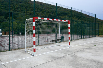 handball or soccer goal on a concrete court closed by a high metal fence - obrazy, fototapety, plakaty