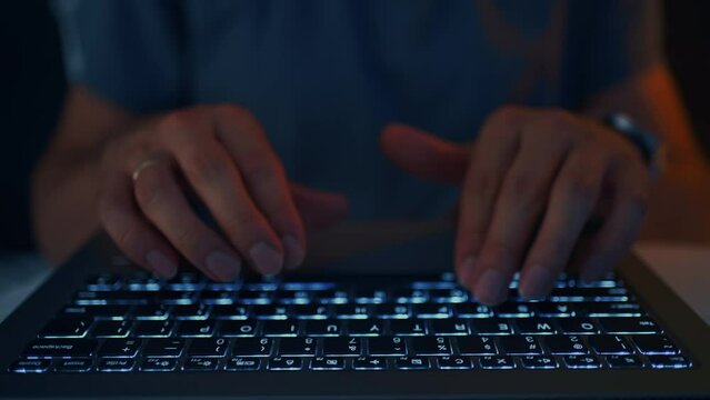 adult man is working with laptop in night, closeup view of hands and keyboard, surfing internet