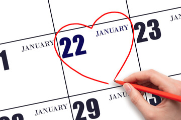 A woman's hand drawing a red heart shape on the calendar date of 22 January. Heart as a symbol of love.