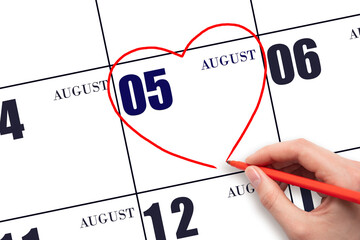 5th day of August. A woman's hand drawing a red heart shape on the calendar date of 5 August. Heart...