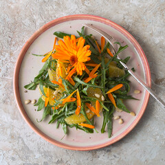 plate with vegetarian salad with arugula, orange and calendula flowers on a light table - obrazy, fototapety, plakaty