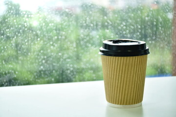 hot coffee in brown plastic cup on glass window in rainy day