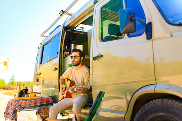 Young man sits on the doorstep of trailer truck and playing guitar