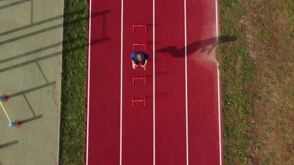 Blond athlete in a blue T-shirt develops his dynamic strength by jumping over hurdles on an athletic oval. 4k video
