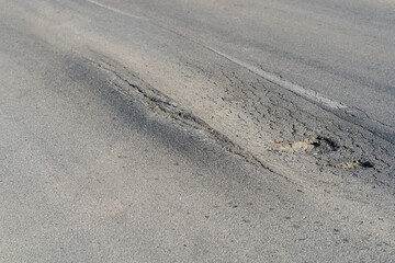 Broken road with holes and cracks built in countryside on hot sunny day. Deformed and expanded asphalt surface with potholes caused by heavy overloaded trucks driving on highway at rural site closeup