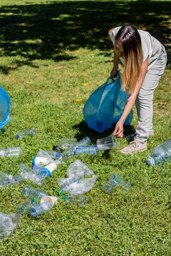 Portrait of a young asian woman collecting plastic bottles in a park for recycling and help the planet, vertical image
