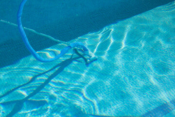 A manual pool cleaner under the waters of the blue tile pool. Pool cleaning and maintenance.