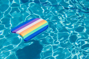 An isolated pool float of colorful lines floating on a sunny day in a tiled pool filled with water. Summer and vacations.