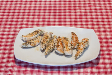 Presentation on a white plate of a delicious recipe for tender rosemary chicken tenderloins on a red checkered tablecloth.