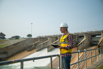 Portrait of engineer wearing yellow vest and white helmet with tablet Working day on a water dam...