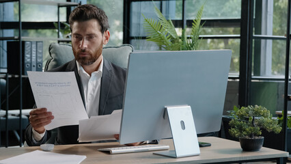 Serious adult 40s bearded pensive thoughtful businessman working at computer in office with...