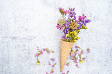 Graphic resource of an ice cream cone filled with dried statice flowers and starflower seed pods. A sprinkle of statice flowers around the cone. Concrete background. Space for text.