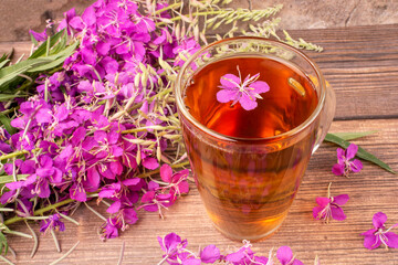 Fototapeta na wymiar A drink (decoction) from the leaves and flowers of a useful plant of ivan-tea (kipreya, epilobium) in a transparent glass mug. Phytotherapy, herbal treatment.