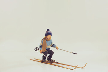 Portrait of little boy, child in winter clothes, jacket and hat riding on skis isolated over grey studio background. Winter holidays