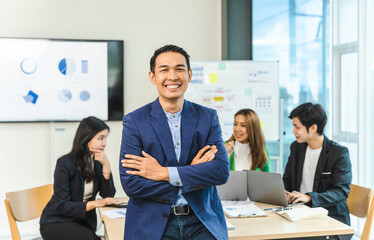 Asian man crossed hands and looking to camera. Group of mixed race start up business people discussing terms of transaction in office.