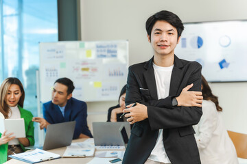 Asian man crossed hands and looking to camera. Group of mixed race start up business people discussing terms of transaction in office.