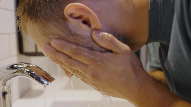 Bearded hipster washes face with water in public toilet
