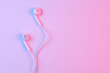 Wired white earphones isolated on white background close-up in pink neon light
