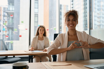 Happy woman shows heart with her hands, sitting in office