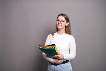 Cute student with glasses holds colorful folders on a gray background