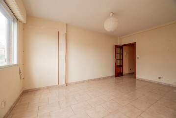 Empty living room of a residential house with pale pink stoneware flooring, cream colored walls and aluminum bay window