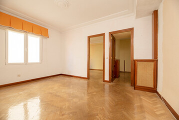 Empty living room of a residential house with French oak parquet flooring placed in herringbone, wood carpentry on the doors and wooden radiator cover and grid