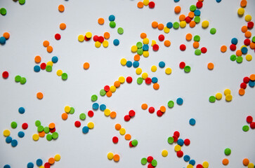 On a white sugar backing lies a sweet pastry topping in the form of pink hearts, orange, turquoise and red peas, and green, blue and yellow sticks