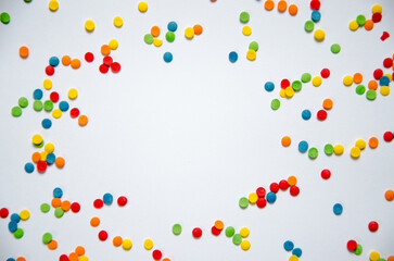 On a white sugar backing lies a sweet pastry topping in the form of pink hearts, orange, turquoise and red peas, and green, blue and yellow sticks