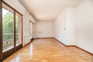 Fototapeta na wymiar Empty living room has oak parquet floor, two balconies with bronze colored aluminum doors, plain white painted walls