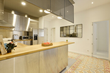 open kitchen, with a long rectangular dining island with wooden countertops and stainless steel cabinets with many stainless steel appliances